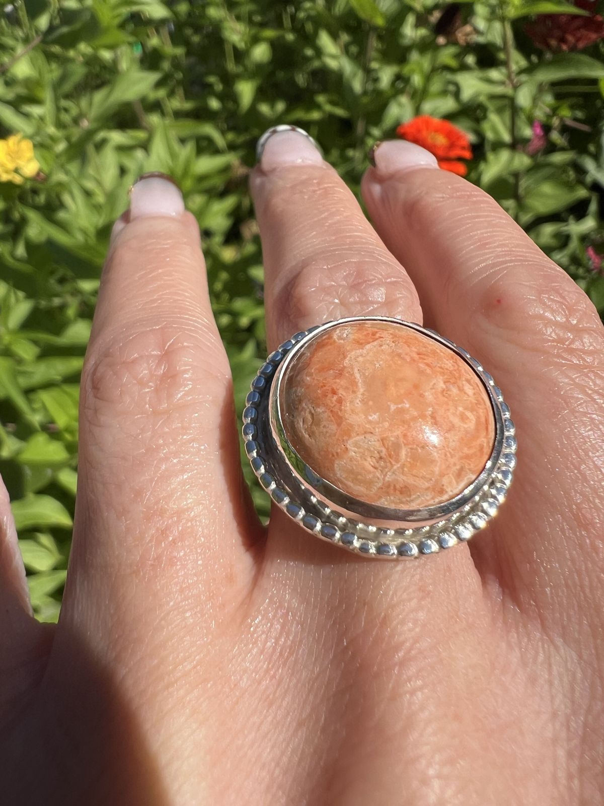An orange cabochon ring in a beaded sterling bezel, worn on the hand in the garden