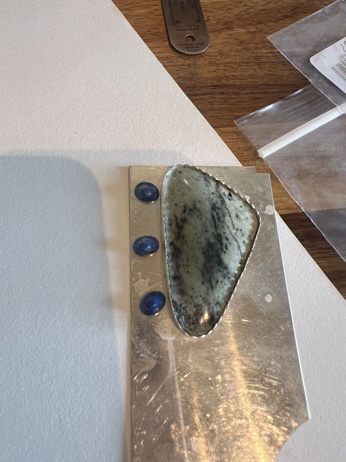 A green stone bezel setting with lapis dots on a soldering plate