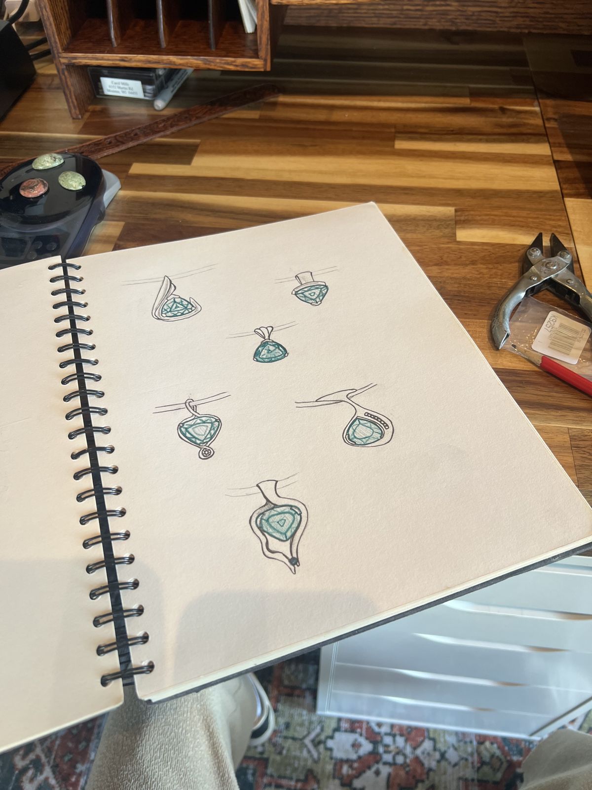A sketchbook page of pendant designs colored teal, on the bench
